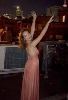 a woman in a long pink dress is posing for the camera with her arms up