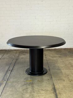 a black round dining table sitting on top of a cement floor next to a white brick wall