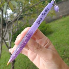 a person holding a purple pen with writing on it in their left hand and a tree in the background