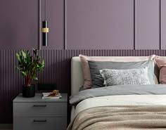 a bed sitting next to a night stand with a plant on top of it in front of a purple wall