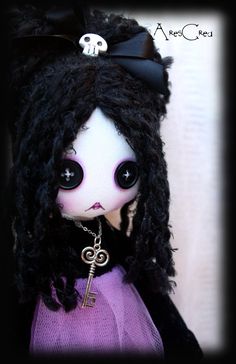 a doll with long black hair wearing a purple dress and holding a key to her chest