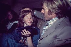 a man and woman sitting in the back of a car looking at an electronic device