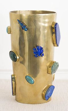 a gold vase with blue and green decorations on the outside, in front of a white wall