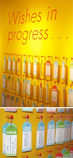 there are many tags hanging on the wall with words written on them, and in front of it is a yellow sign that says wishes in progress