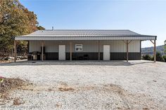 a metal building sitting on top of a gravel field next to trees and mountains in the background