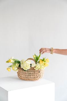 a woman placing flowers in a wicker basket on top of a white countertop