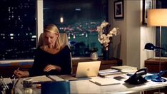 a woman sitting at a desk in front of a laptop computer with a view of the city