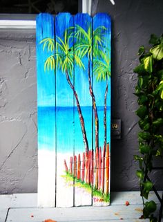 a painted wooden sign with palm trees and the ocean in the background on a porch