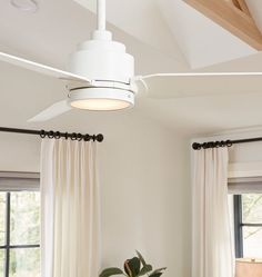 a white ceiling fan hanging from the ceiling in a room with two windows and curtains