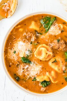 a white bowl filled with tortellini soup next to a spoon and bread on the side