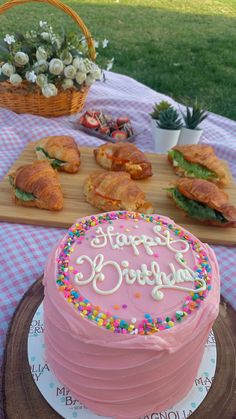 a pink birthday cake sitting on top of a table next to other foods and desserts