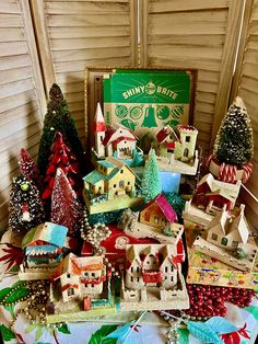 a table topped with lots of small christmas trees next to a box filled with tiny houses