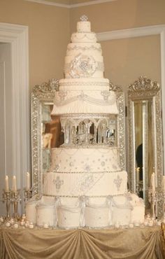 a large white wedding cake sitting on top of a table next to a mirror and chandelier