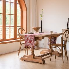 a wooden table with two chairs and a vase on it in front of a window