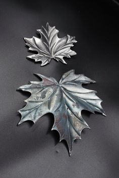 two metal leaves sitting on top of a black table next to each other and one is silver