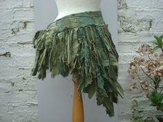 a mannequin with green leaves on it's skirt and white brick wall in the background