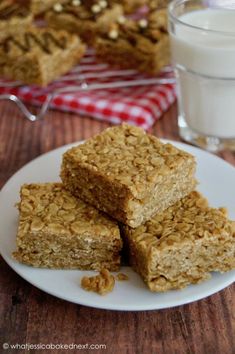 three pieces of granola bars on a plate next to a glass of milk