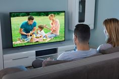 a man and woman sitting on a couch watching tv with their child in front of them