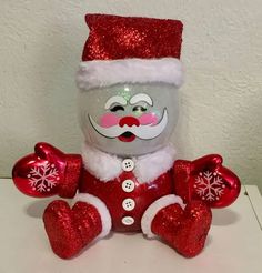 a stuffed animal wearing a santa claus hat and holding two red heart shaped christmas ornaments