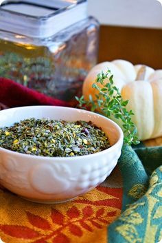 a white bowl filled with herbs on top of a table next to some pumpkins