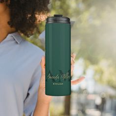 a woman holding up a travel mug with the words emerald valley in gold on it