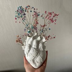 a hand holding a vase with flowers in it and an artificial heart on the side