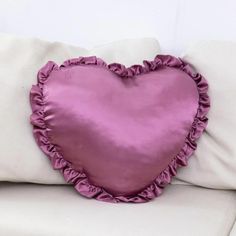 a heart shaped pillow on top of a white couch with purple ruffled trims