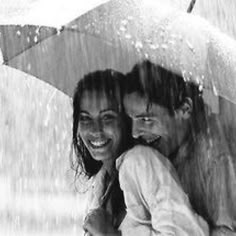 black and white photograph of two people under an umbrella in the rain, one smiling at the camera