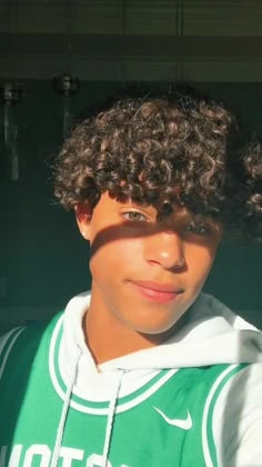 a young man with curly hair wearing a green and white hoodie