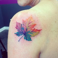 a colorful maple leaf tattoo on the back of a woman's left upper arm