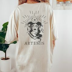 Get ready to be OBSESSED with your new Artemis Greek Mythology shirt. It's the cutest and most trendy way to combine all those important trendy light academia and greek apparel vibes! This is the perfect mythology shirt!  * Q U I C K * F A C T S * ✺  All shirts are UNISEX ✺  100%  ringspun cotton (fiber content may vary for different colors) ✺  Soft-washed, garment-dyed fabric brings extra coziness ✺  Wash and dry normally (on cool for best results) ✺  Sewn-in twill label * S I Z I N G * ✺ For an oversized fit, select two or three sizes up from your normal size ✺ Model is wearing size L  ✺ Sizing runs true to size ✺ Relaxed fit ✺ Most women find their typical size works best, since they are meant to fit a touch loose ✺ See Size guide and fit in images          * S H I P P I N G * T I M E S Artistic Relaxed Fit Shirt With Screen Print, Relaxed Fit Graphic Print Shirt In Bookish Style, Relaxed Fit Graphic Print Shirt With Bookish Style, Bookish Cotton Shirt With Graphic Print, Artemis Greek Mythology, Goddess Mythology, Greek Letter Shirts, Artemis Goddess, Poet Shirt