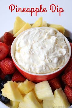 a bowl filled with fruit and dip surrounded by sliced pineapples, strawberries, and blueberries