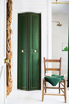 a room with a green door and wooden chair in the foreground, next to a white wall