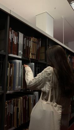 a woman is picking up some books from a book shelf in a library with other books on the shelves