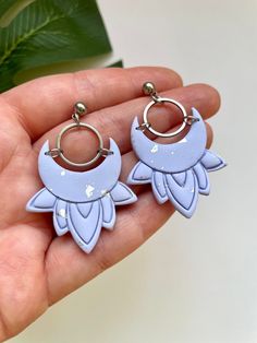 a person holding two small blue earrings in their left hand, one with an owl on it's ear