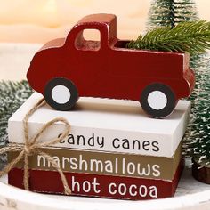 a red toy truck sitting on top of three books with christmas trees in the background