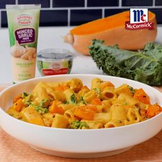 a bowl filled with pasta and vegetables next to a carton of macaroni and cheese