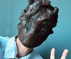 a man wearing a brown leather mask with his hand up to the face and fingers in front of him