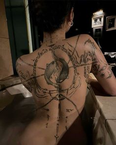 a woman with tattoos on her back sitting in a bathtub