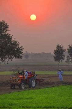 two men are plowing the field with their farm equipment as the sun sets in the background