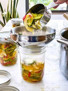 a person scooping pickles out of a jar into the other jars on a table