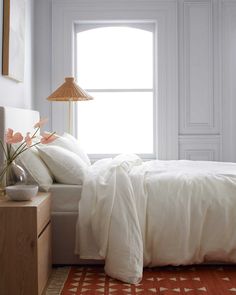 a bed with white sheets and pillows in a bedroom next to a lamp on a dresser