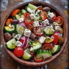 a wooden bowl filled with cucumbers, tomatoes and other vegetables on top of a table