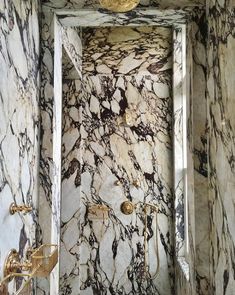 a bathroom with marble walls and flooring next to a bathtub filled with gold faucets