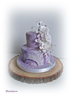 a purple and white wedding cake with flowers on the top is sitting on a tree stump