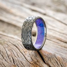 a wedding ring with blue and purple inlays on it sitting on top of a piece of wood