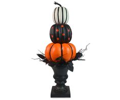 three pumpkins are stacked on top of each other in a black vase with leaves