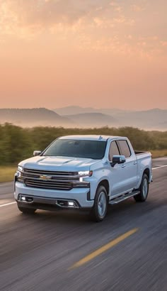 a white truck driving down the road with mountains in the background