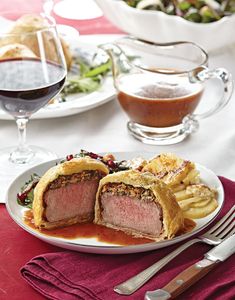 a white plate topped with meat covered in sauce next to a glass of red wine