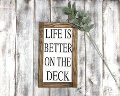 a wooden sign that says life is better on the deck with a flower in it